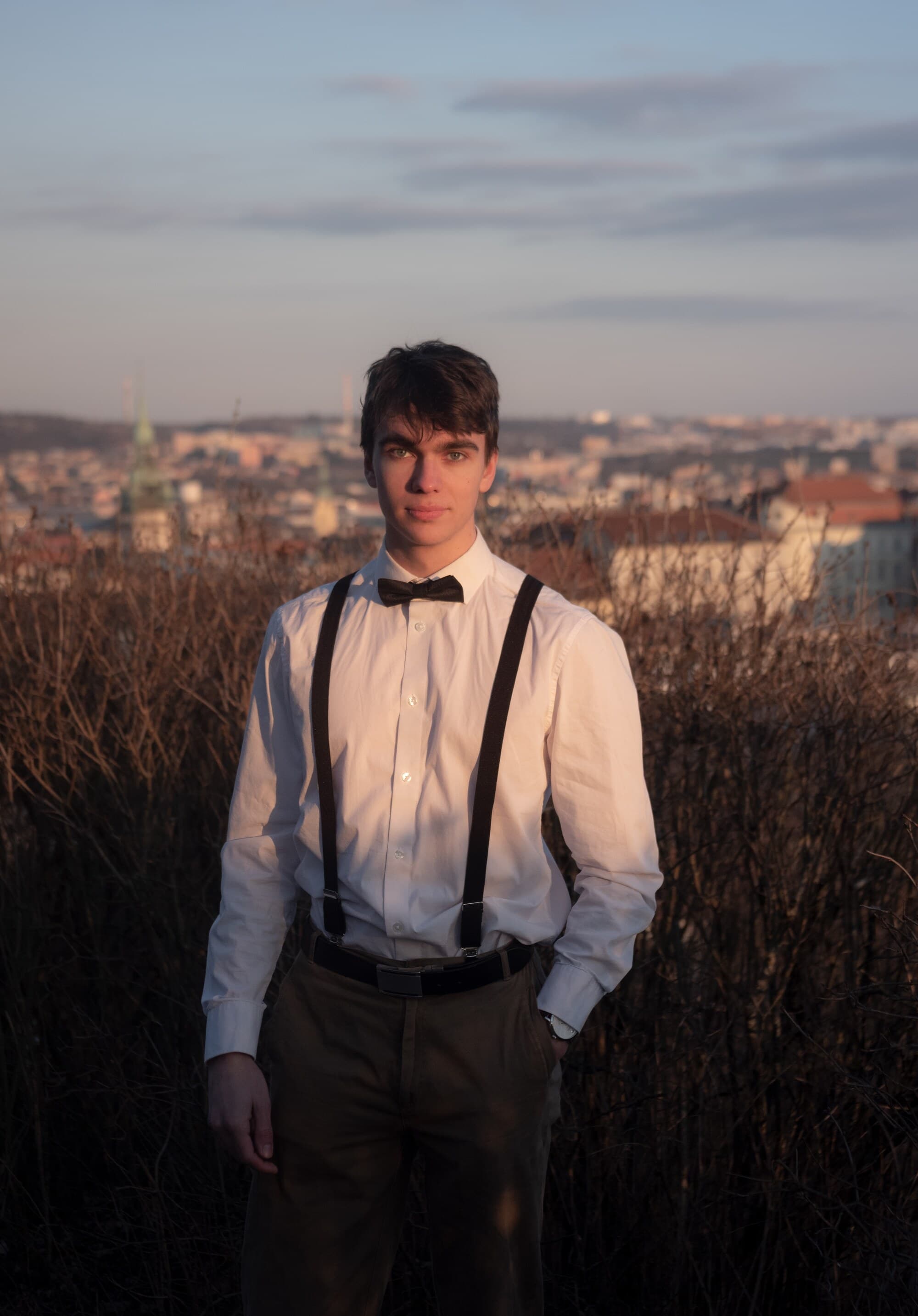 Václav Kozák v bílé košili s motýlkem, za ním panorama Brna při západu slunce